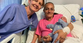 Research Midwife Marie Home posing with new mum Danielle Woodward and her baby son Leif. Danielle is sitting in a hospital bed, holding Leif, while Marie stands alongside them in her work scrubs.