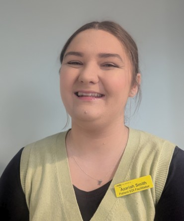 Araziah smiling for the camera while wearing her yellow 'Hello my name is' NHS badge.