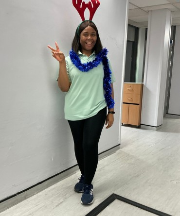 Noella Isibor stood in a corridor and is wearing a domestics uniform, antlers, and blue tinsel.