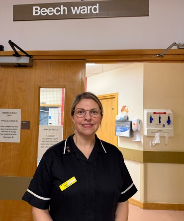 Lyn at the entrance to Beech Ward in her black ward clerk uniform.