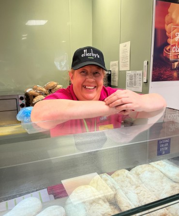 Jenny standing behind a deli counter, wearing her Ellerby's hat and smiling.