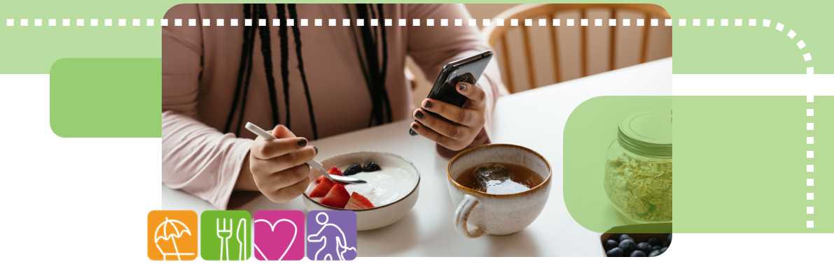 Image of person looking at phone while eating fruit from bowl at table