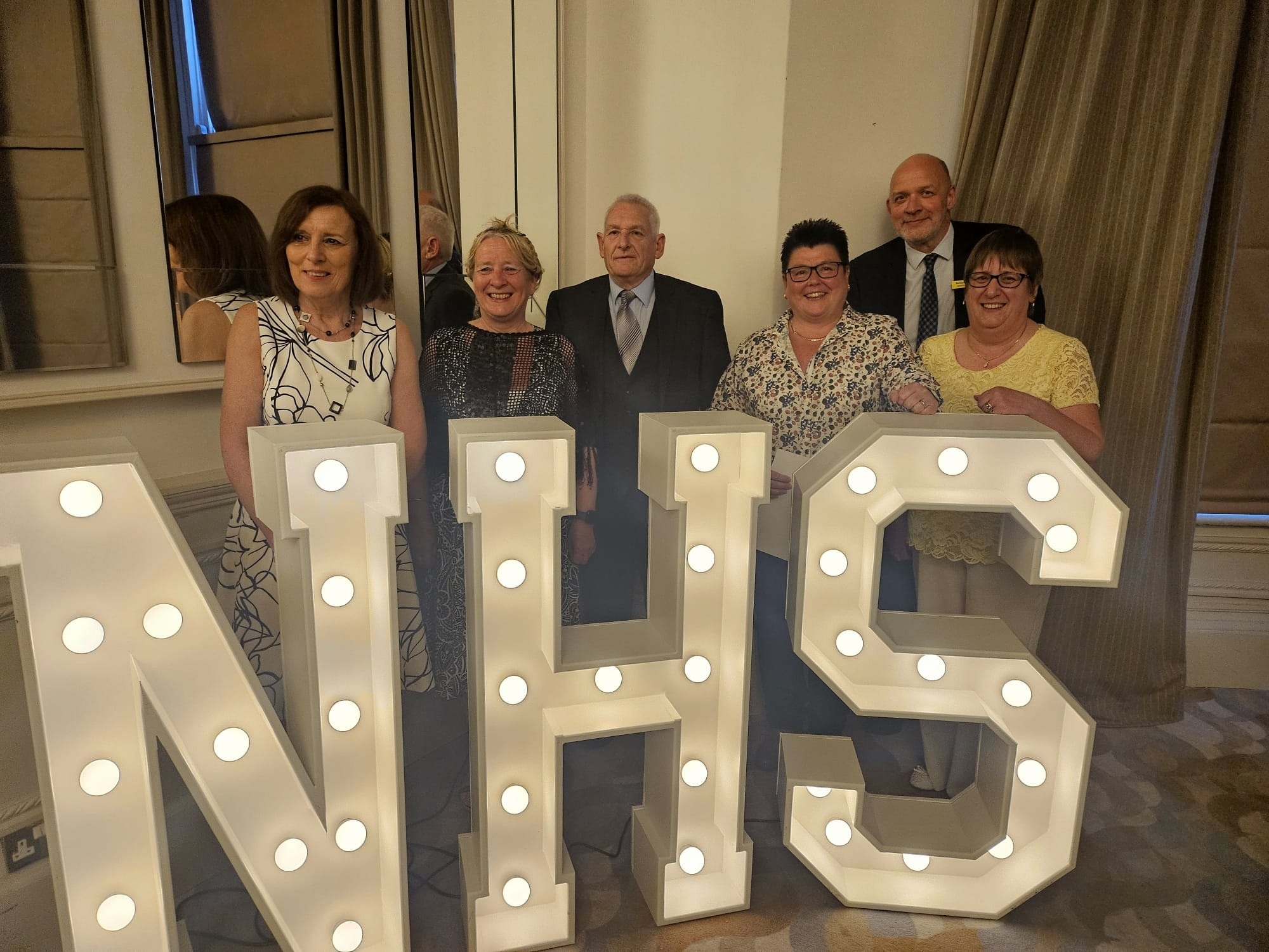 NHS staff standing together behind giant letters that spell NHS.